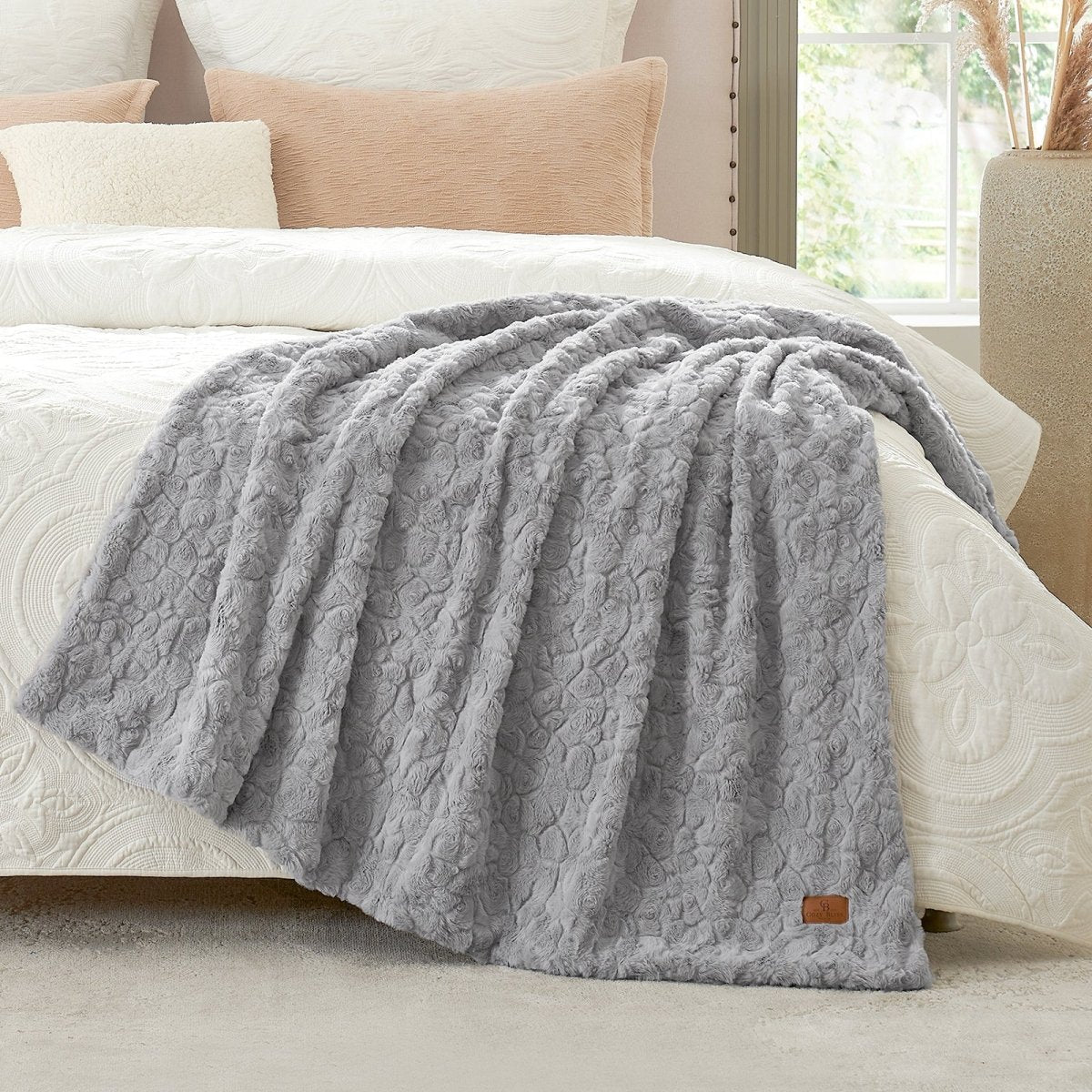 Grey textured blanket on a bed with beige pillows and a lamp in the background #color_Grey