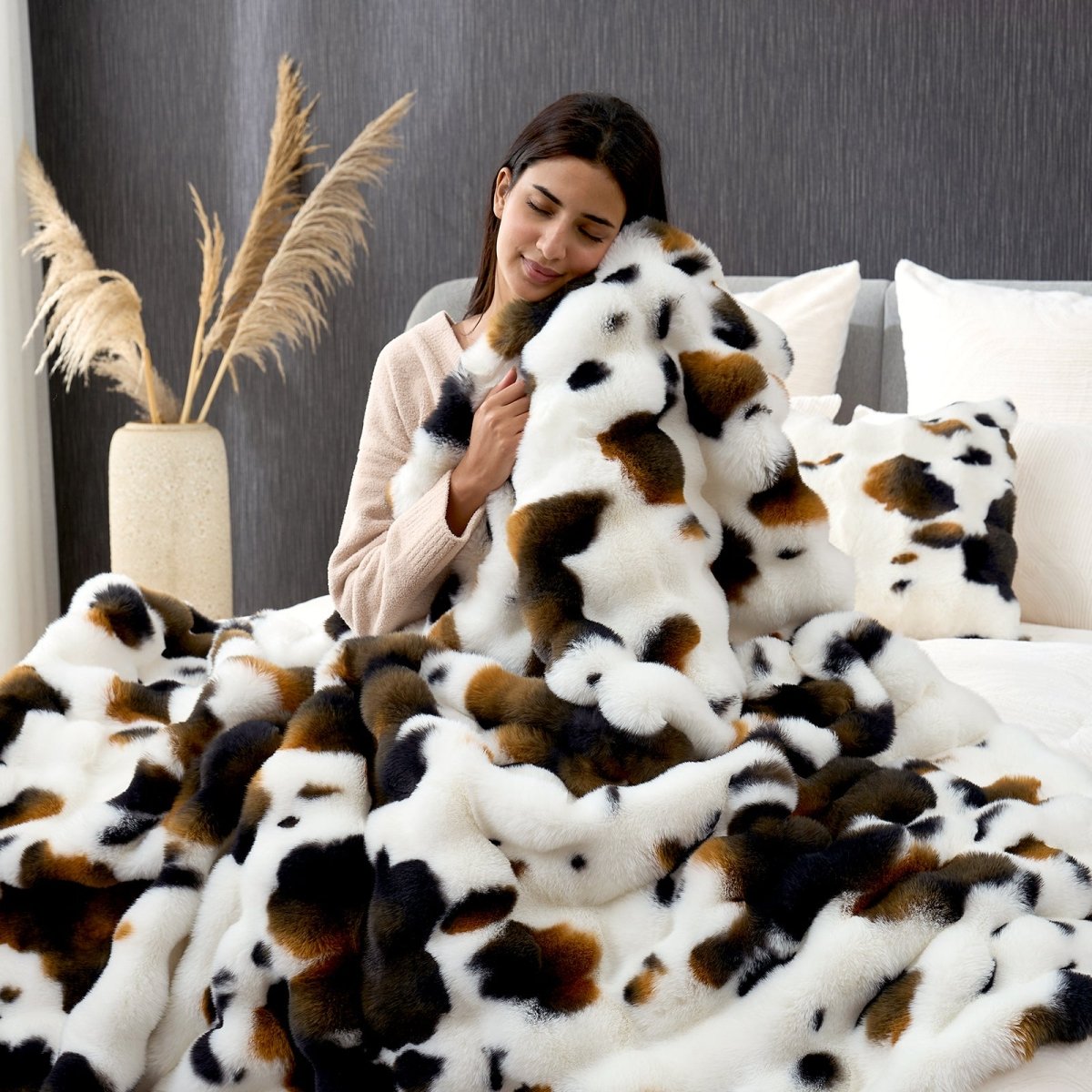 Woman wrapped in a fluffy cow print faux fur blanket on a bed. #Color_Cow Print