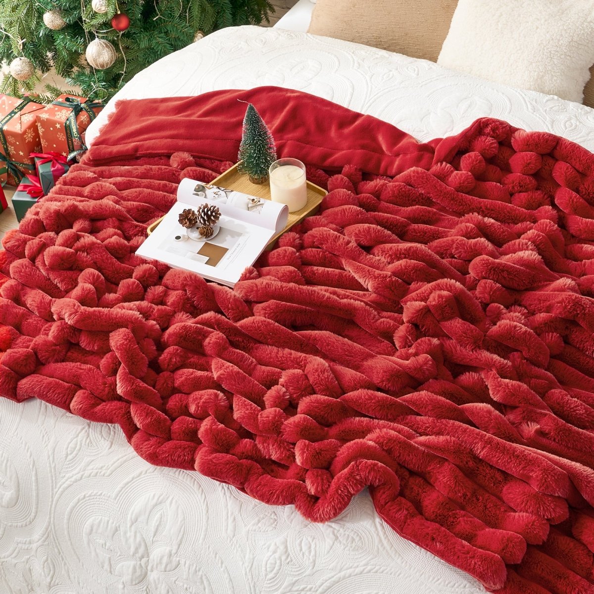 Red textured blanket draped over a surface with a Christmas tree and presents in the background. #color_Christmas Red